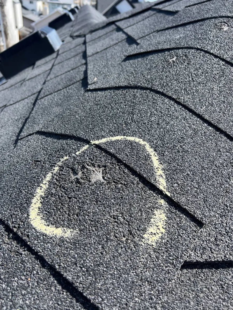 A hail bruise on an asphalt shingle circled in chalk, granules knocked loose