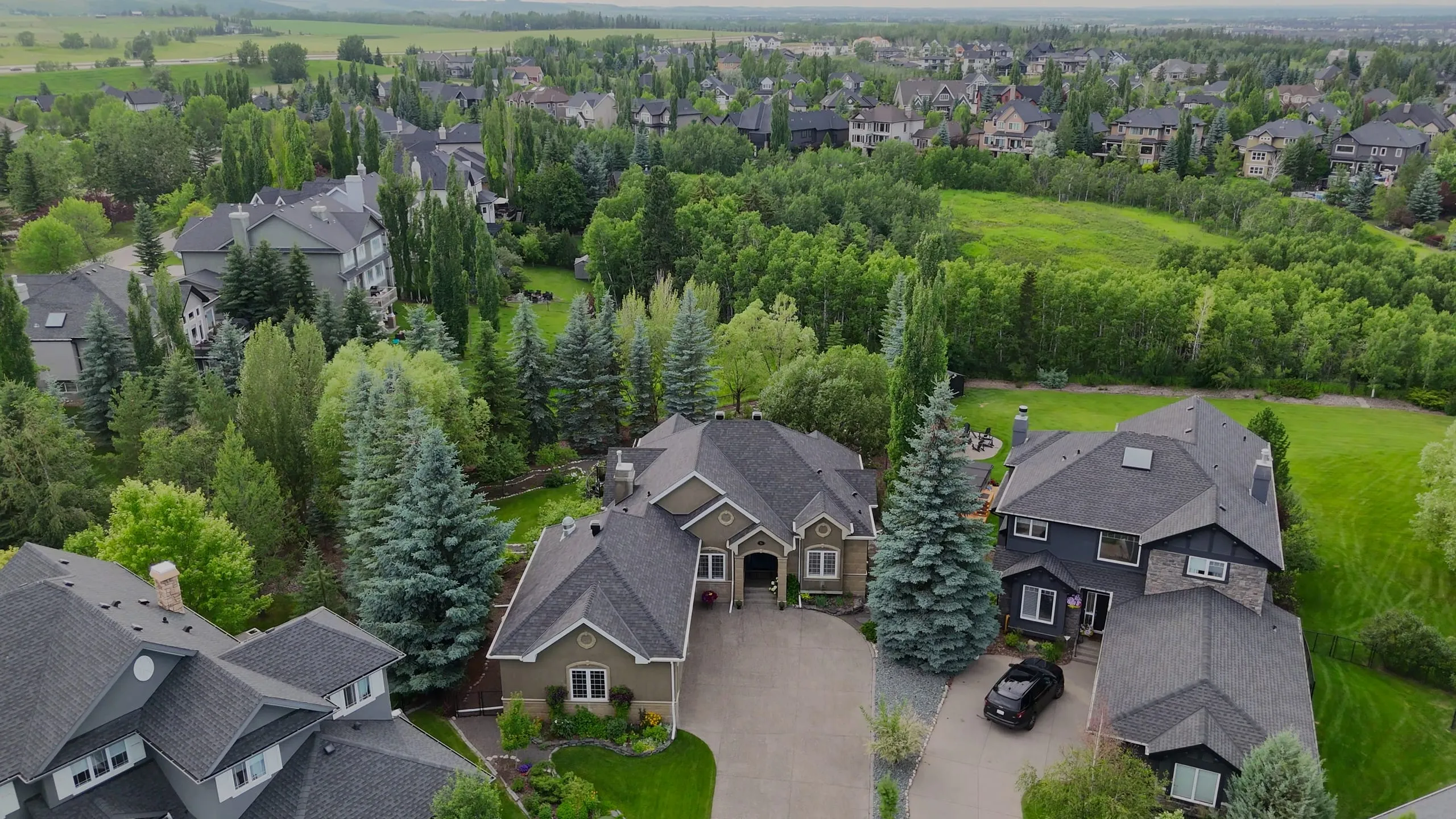 Aerial view of a Calgary home with a new asphalt shingle roof, backing onto trees